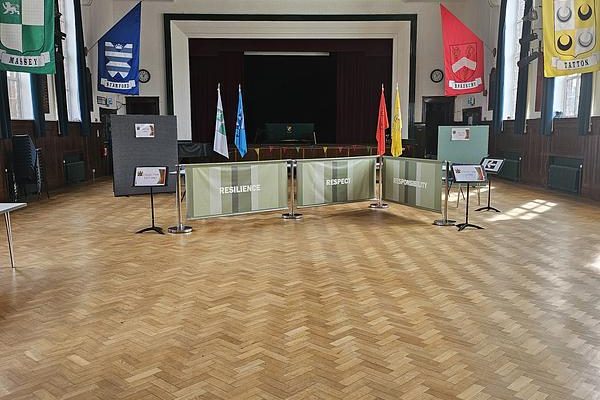 A traditional school hall with a stage at the far end, parquet floor and house banners