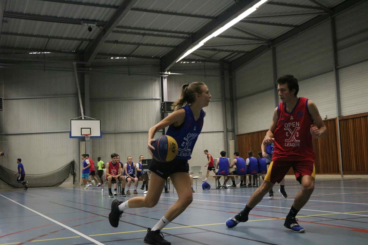 A basketball game in progress inside a school sports hall with marked courts