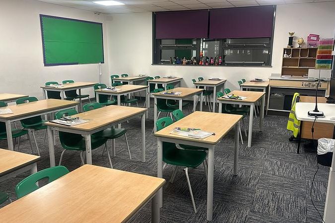 A bright empty classroom with rows of desks, chairs and a green board